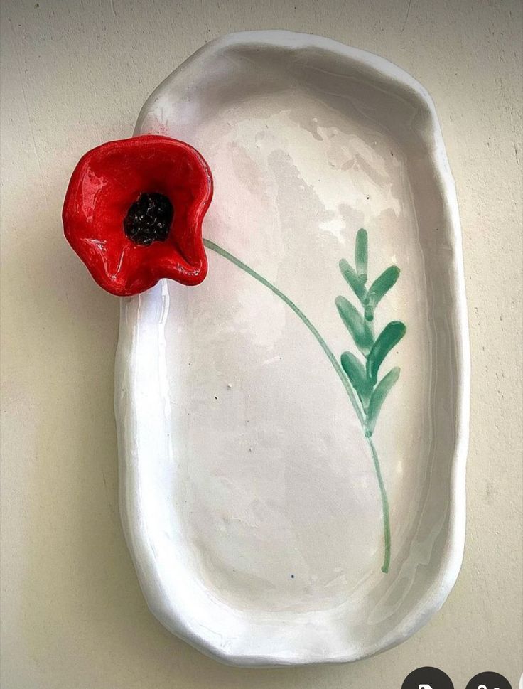 a red flower sitting on top of a white plate with watercolors painted on it