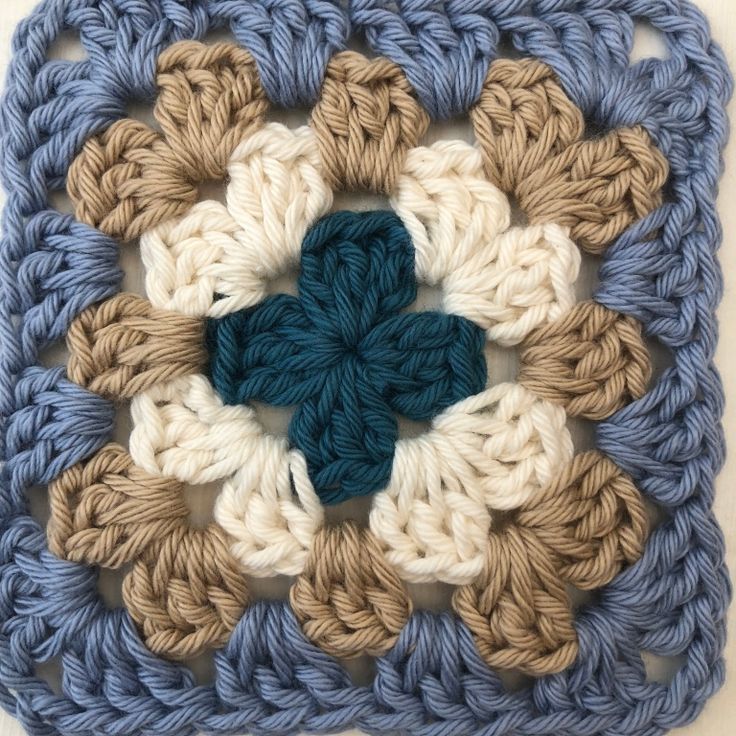 a crocheted square with a blue and white flower on the center is shown