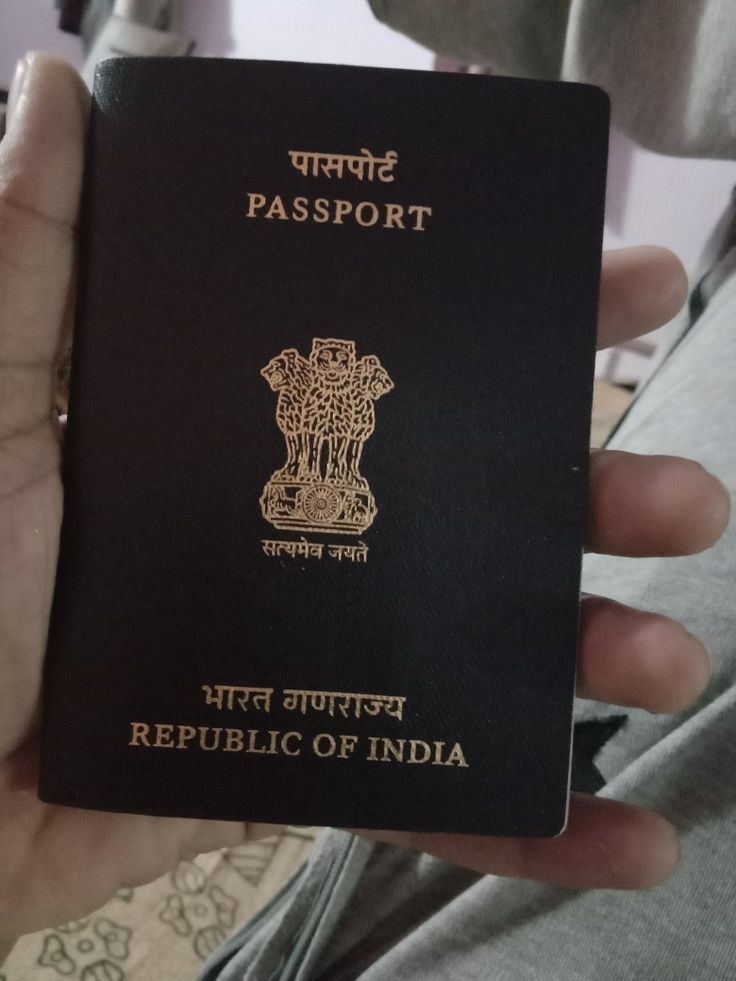 a person holding up a black passport in their hand with the word india written on it