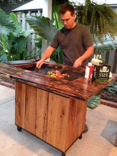 a man is preparing food on top of a wooden table in front of some plants