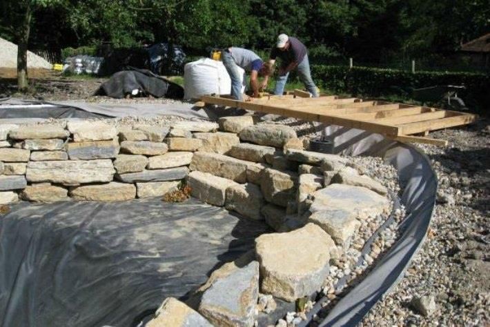 two men working on an outdoor area made out of rocks and wood with tarp covering the ground