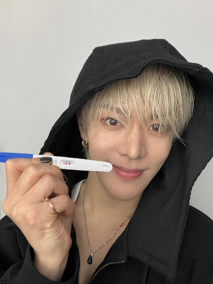 a person with blonde hair holding a toothbrush in front of their face and wearing a black hoodie