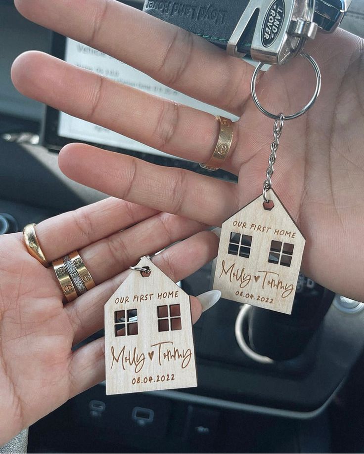 two wooden house keychains are being held by someone's hand in the car