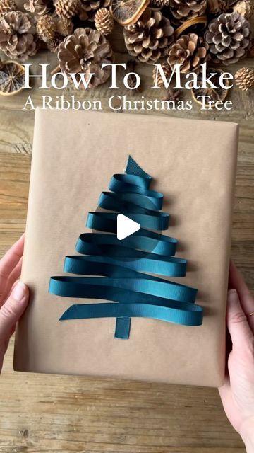 someone holding a wrapped present with blue ribbon on it and the words how to make a ribbon christmas tree