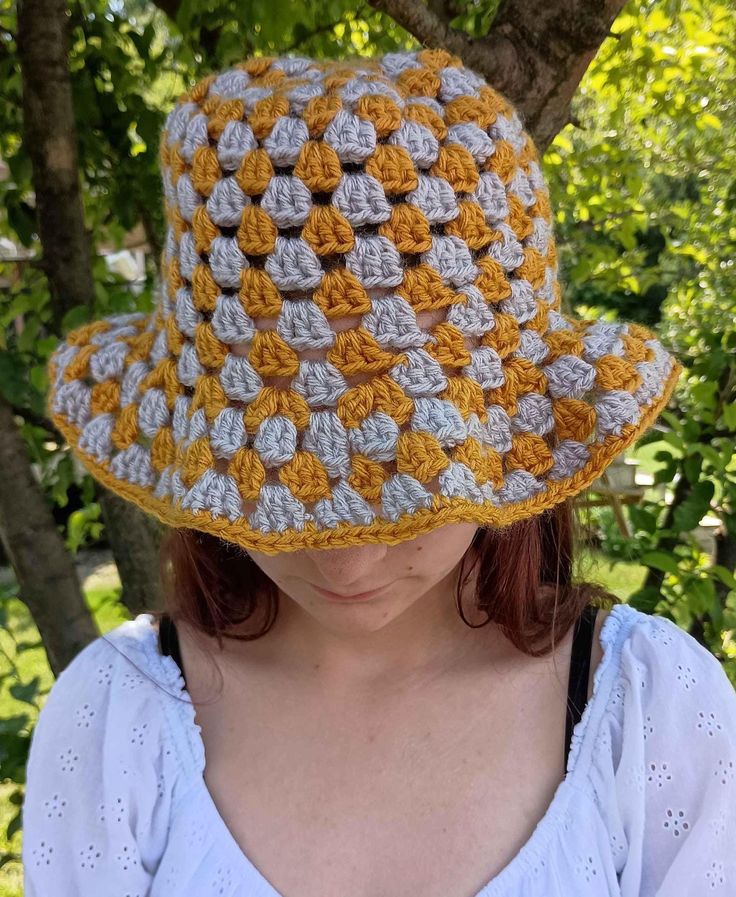 a woman wearing a yellow and gray crocheted hat in front of a tree