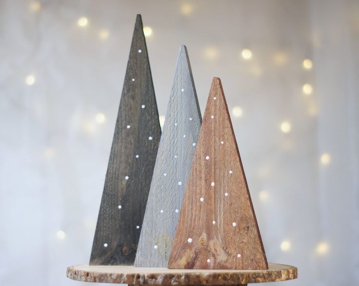 three wooden christmas trees sitting on top of a table next to a white wall with lights