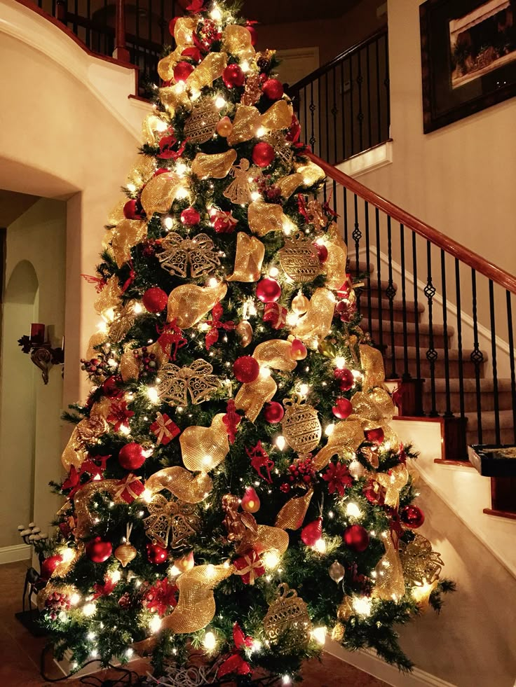 a decorated christmas tree with gold and red ornaments in the corner next to a stair case