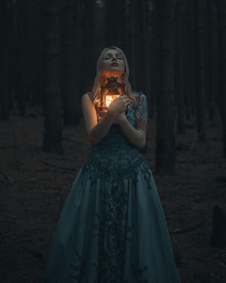 a woman in a blue dress holding a lantern with her face illuminated by the light