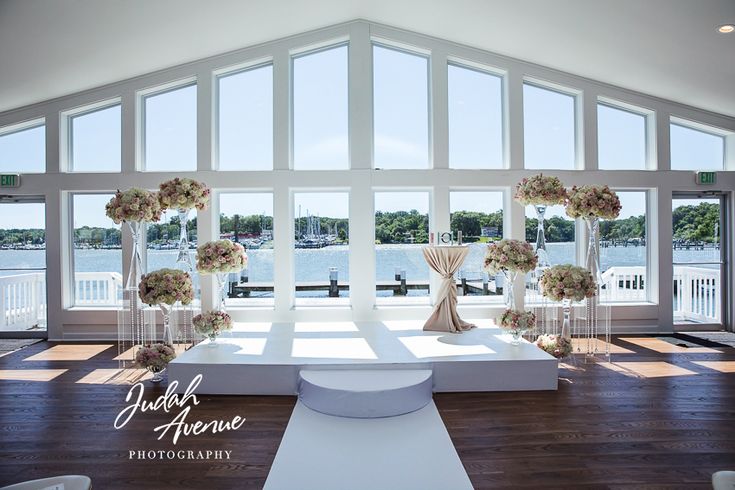 a large room with white furniture and flowers on the tables in front of windows that look out onto water