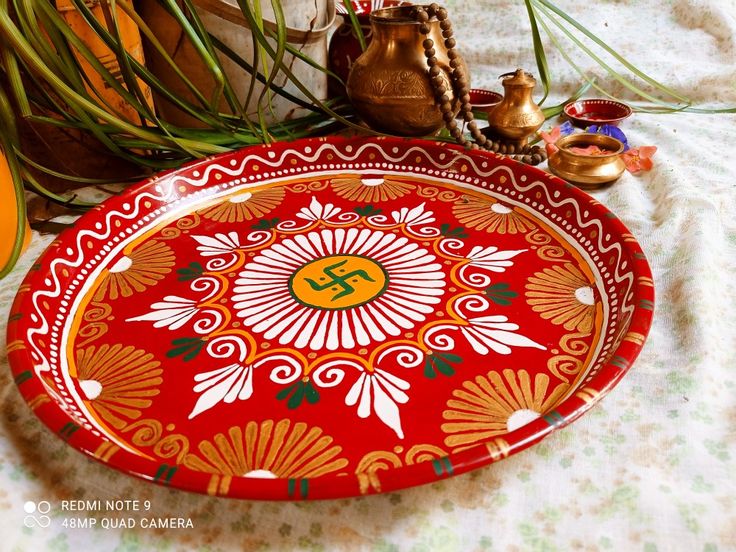 a red and gold plate sitting on top of a table next to potted plants