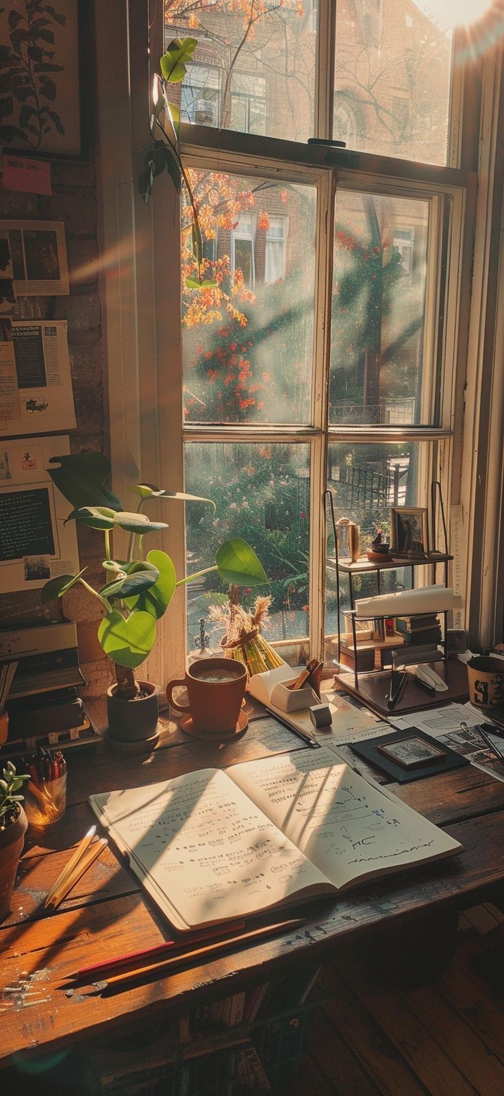 an open book sitting on top of a wooden table next to a window filled with plants