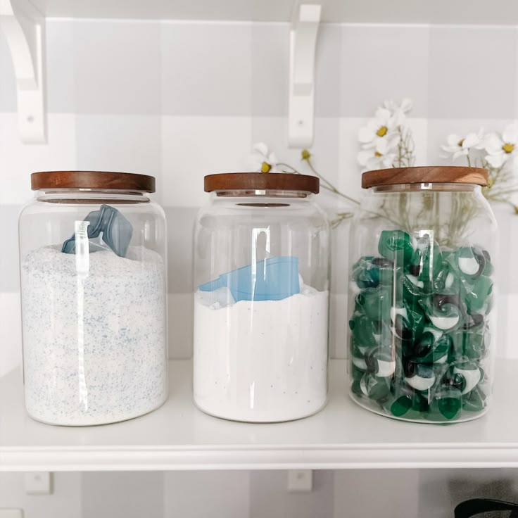 three glass jars filled with different types of rocks and seaglass on top of a shelf