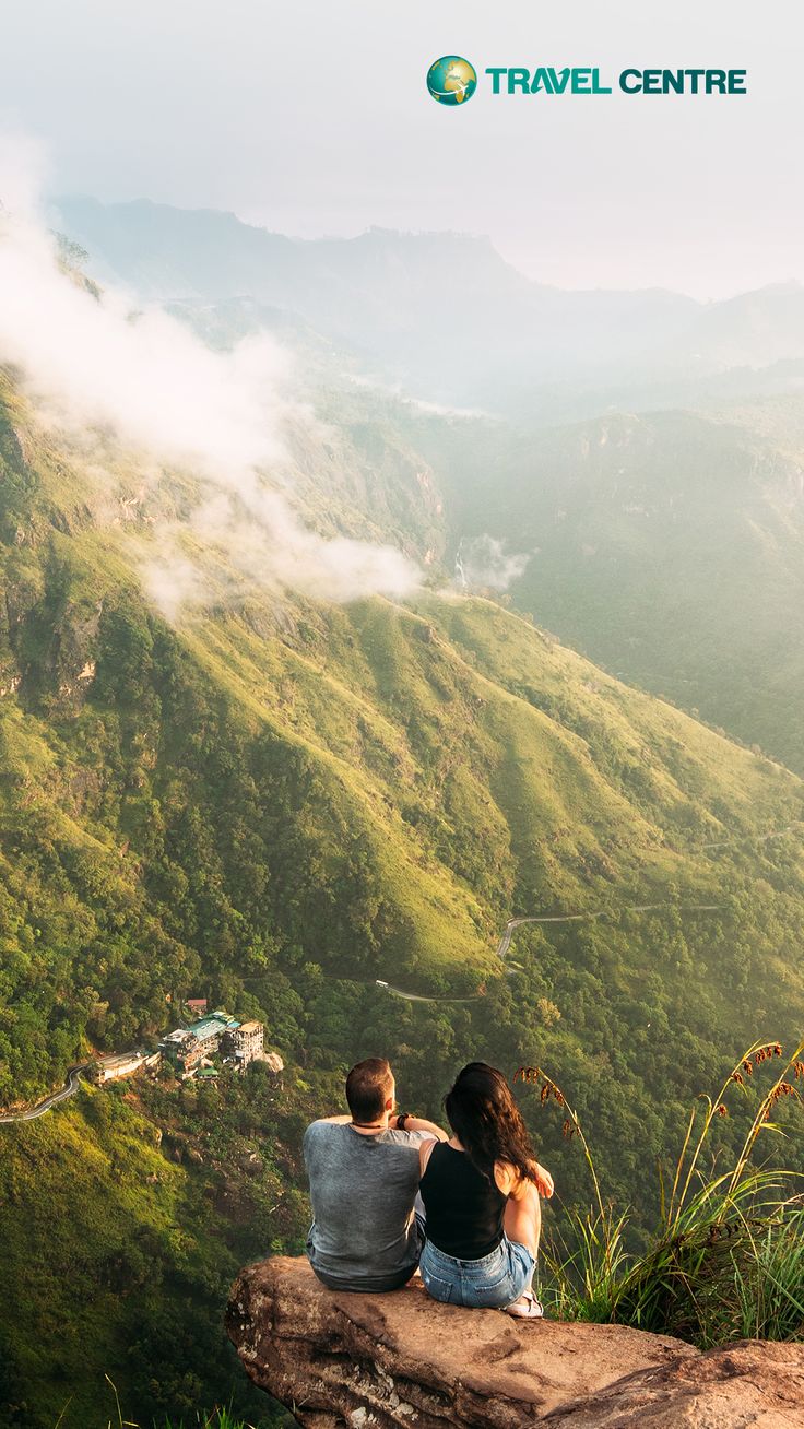 two people sitting on top of a cliff looking at the mountains