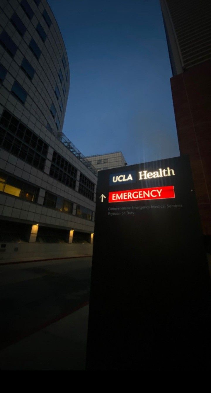 a hospital sign in front of a building at night with the lights on and buildings lit up behind it