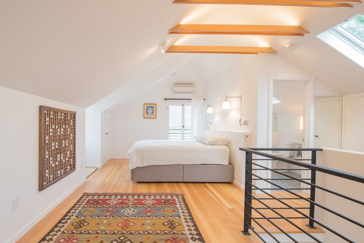 an attic bedroom with hardwood floors and white walls, along with a large rug on the floor