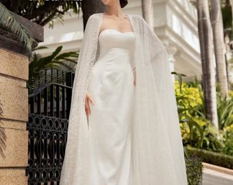 a woman wearing a white wedding gown with a long cape on her head and shoulders