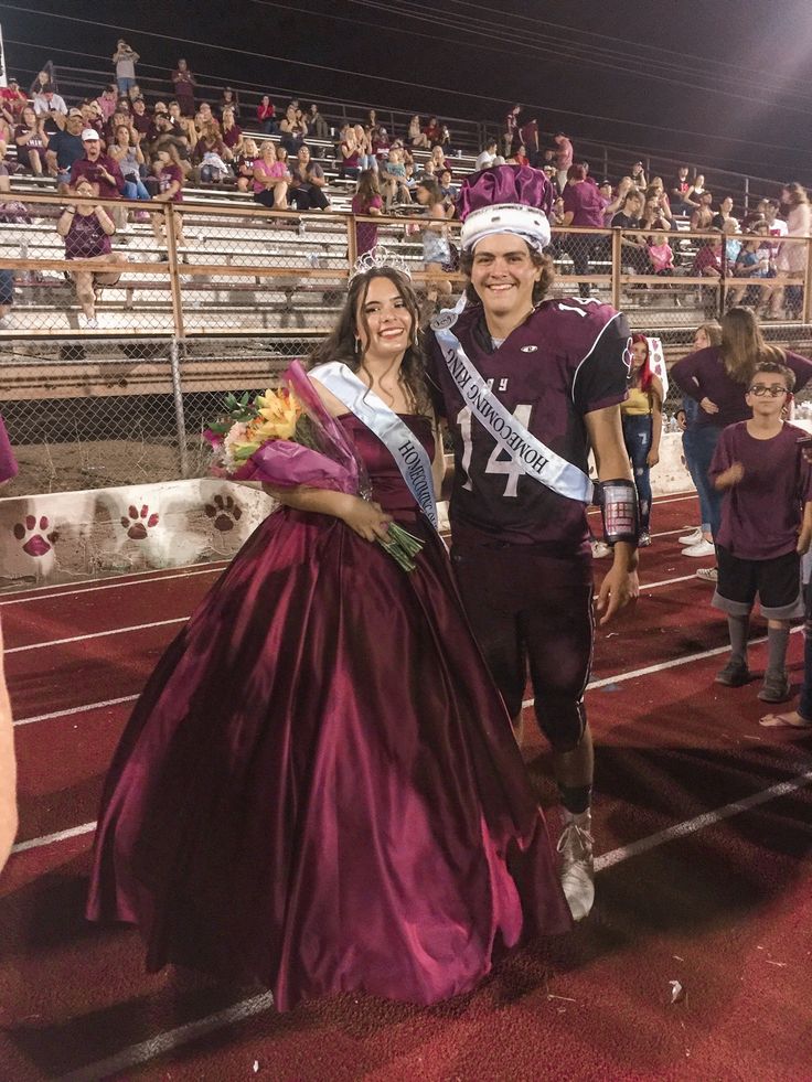 a man and woman in purple dresses standing next to each other at a football game