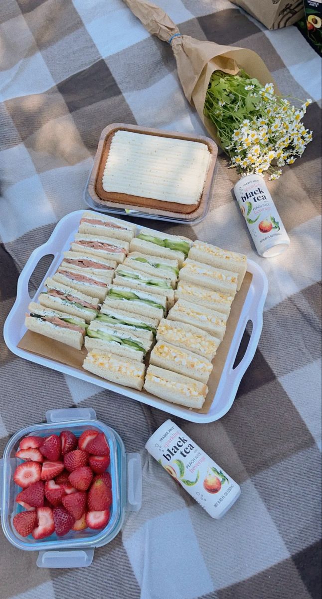 sandwiches and strawberries on a picnic table with other food items including yogurt