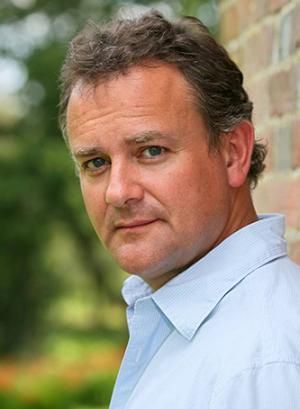 a man in a blue shirt leaning against a brick wall with his head turned to the side