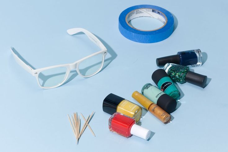 various nail polish and eyeglasses on a white surface next to a blue tape