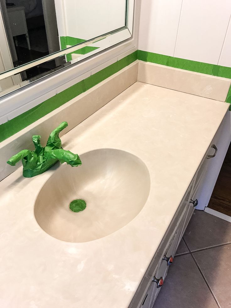 a white sink sitting under a bathroom mirror next to a green leafy plant on top of a counter