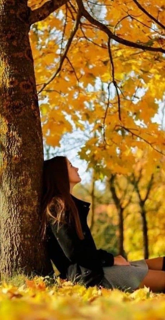 a beautiful young woman sitting under a tree in the fall season with her eyes closed