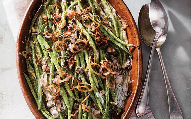 a wooden bowl filled with green beans covered in onions and onion dressing next to two spoons