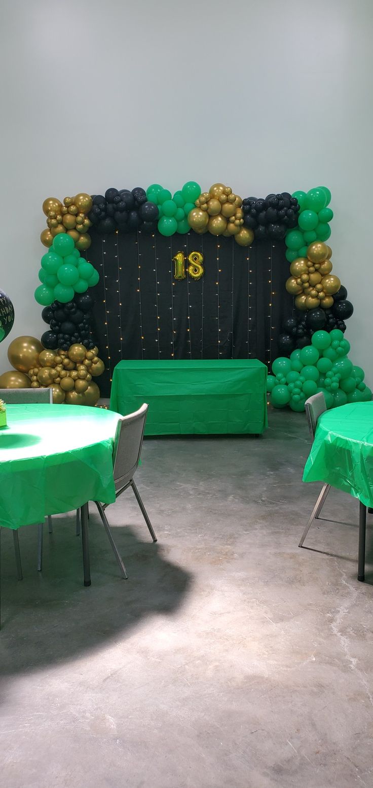 a room with green and black balloons on the wall, tables and chairs in front of it