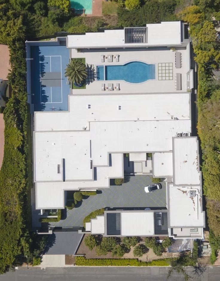 an aerial view of a house with a swimming pool and tennis court in the foreground