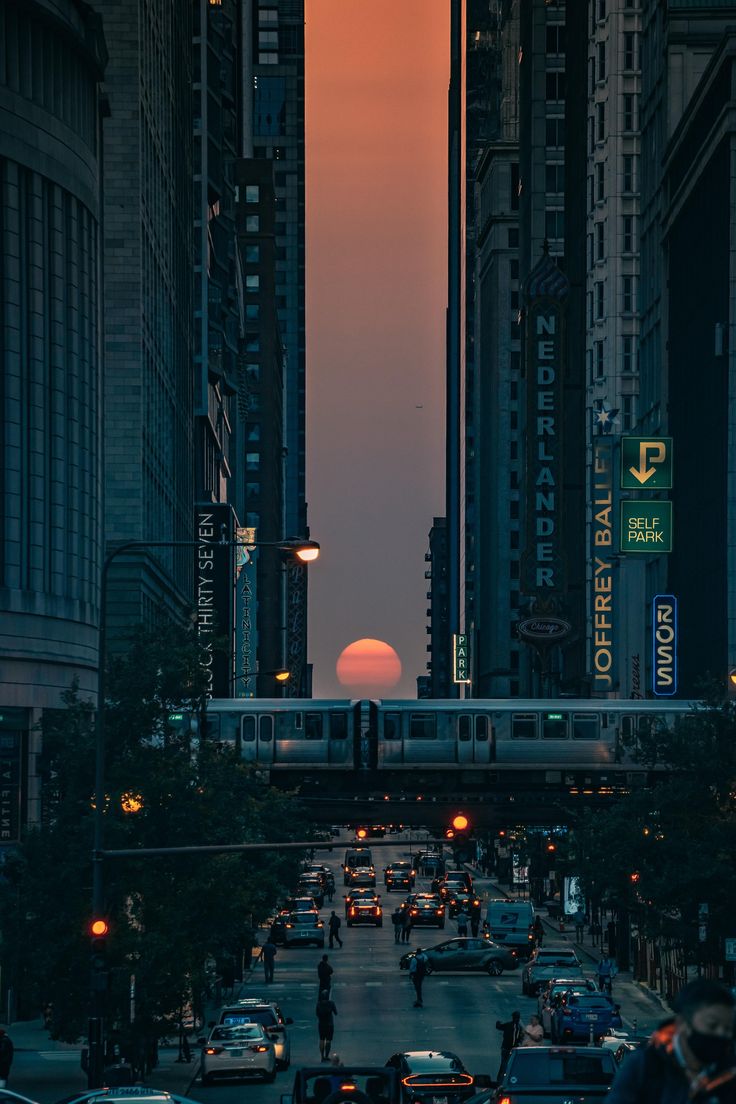 the sun is setting behind tall buildings in an urban area with cars driving down the street