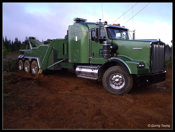 a large green truck parked on top of a dirt field next to a power line