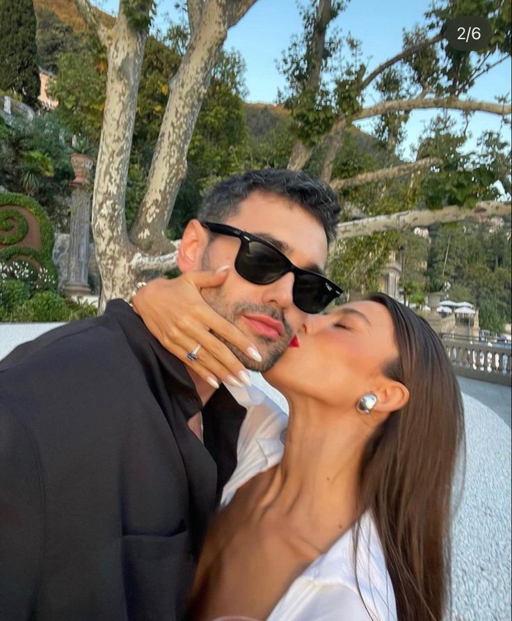 a man and woman kissing each other in front of trees with sunglasses on their heads