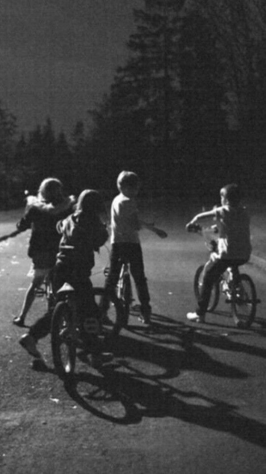 black and white photograph of children riding bikes in the street at night with full moon behind them