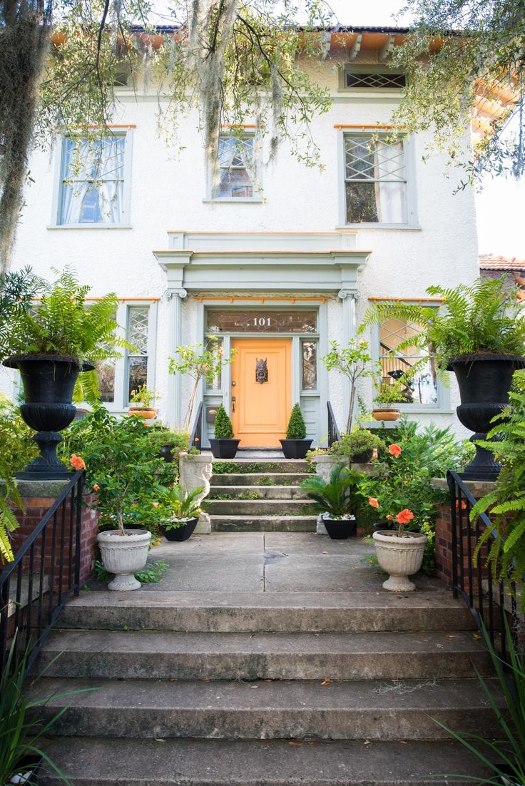 a white house with potted plants on the front steps and stairs leading up to it