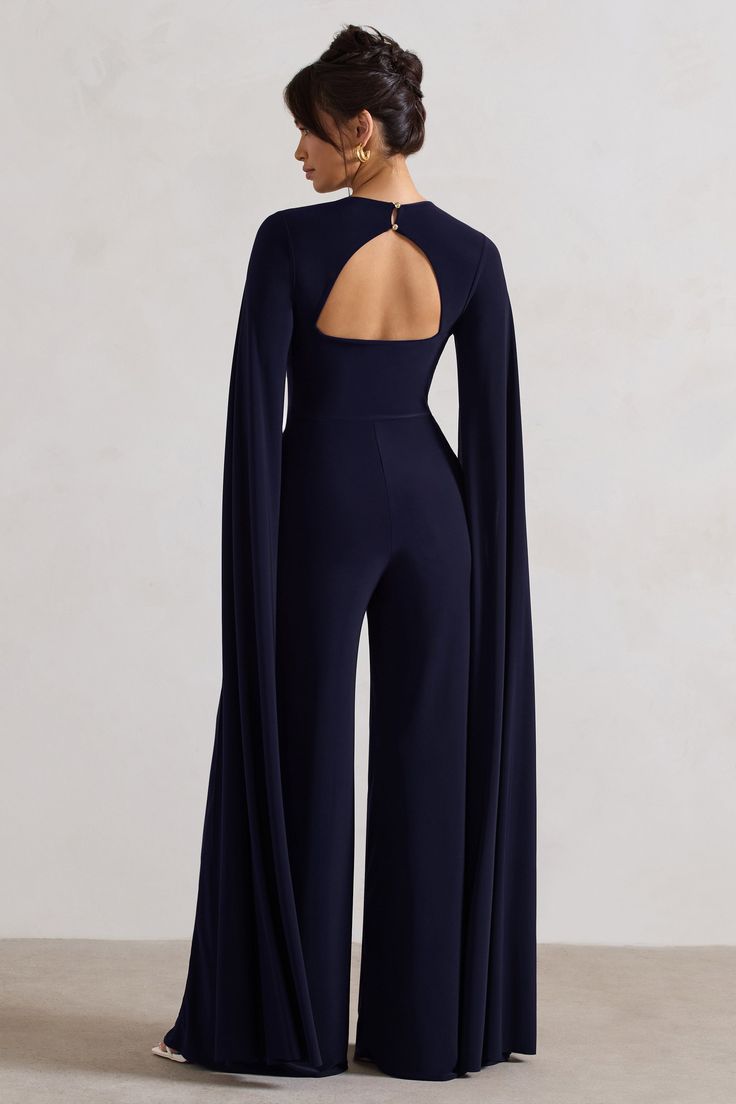 One of our favourite statement jumpsuits of the season, Emmanuela is an elegant ensemble for any formal event. Boasting a sculpting plunge neckline, what defines this flattering navy piece is floor sweeping cape sleeves and a contemporary cut-out back detail. For the perfect graduation look, team yours with some court shoes like Blade. Features - Premium stretch jersey- Plunge neckline - Cape sleeves- Button closure - Back cut out- Wide leg Sizing & Fit Model is 5'8 and wears UK size 8 / US size Fancy Jumpsuit Classy, Navy Jumpsuit Outfit Wedding, Formal Dresses For Graduation, Elegant Jumpsuits For Women, Jumpsuit Elegant Chic Classy, Outfits For The Club, Graduation Jumpsuit, Graduation Outfit Ideas For Guest, Graduation Looks