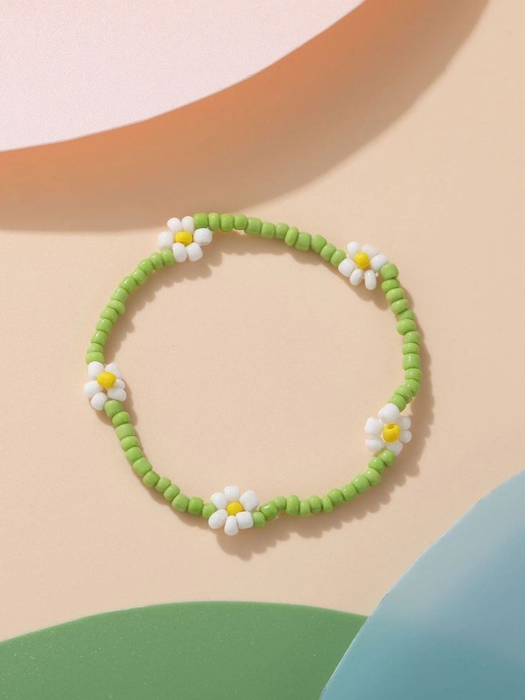 a green beaded bracelet with white and yellow flowers sits on a pastel background