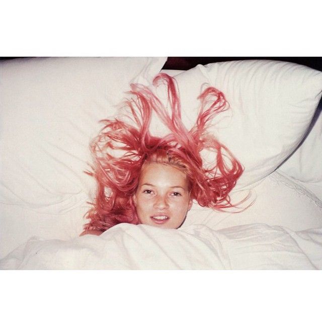 a woman laying in bed with red hair on top of her head and white sheets