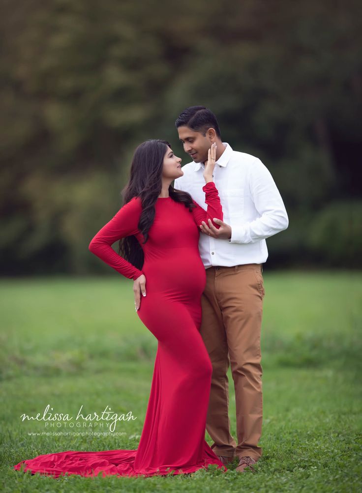 a pregnant woman in a red dress standing next to a man wearing a white shirt and tie