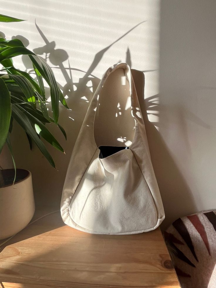 a white purse sitting on top of a wooden table next to a potted plant