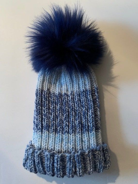 Cute and fashionable knitted hat made with the softest yarn in a warm thick-stitch knit. Acrylic/alpaca/wool/viscose. Topped with a large blue faux-fur pompom. Blue Warm Beanie One Size, Warm Blue Beanie One Size, Blue Winter Hats One Size Fits All, Blue One-size Winter Hats, Blue Hand Knitted Beanie For Winter, Winter Blue Hand Knitted Beanie, Blue Crochet Hat For Cold Weather, Blue Soft Knit Hat For Fall, Blue Yarn Crochet Hat For Winter