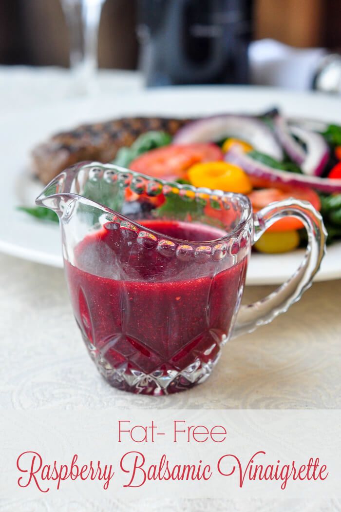 a glass pitcher filled with raspberry balsamic vinaigrete next to a plate of vegetables