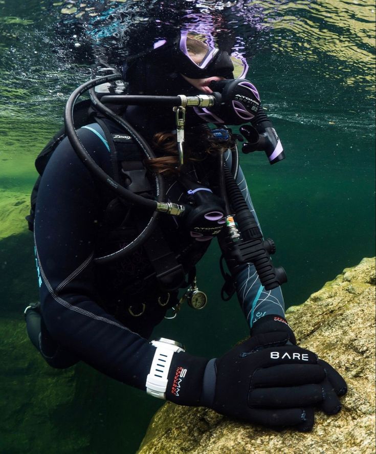 a person wearing scuba gear and diving in the water with their hands on a rock