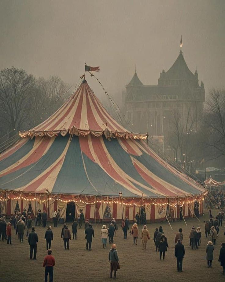 a large circus tent with people walking around it in the foggy day at an amusement park