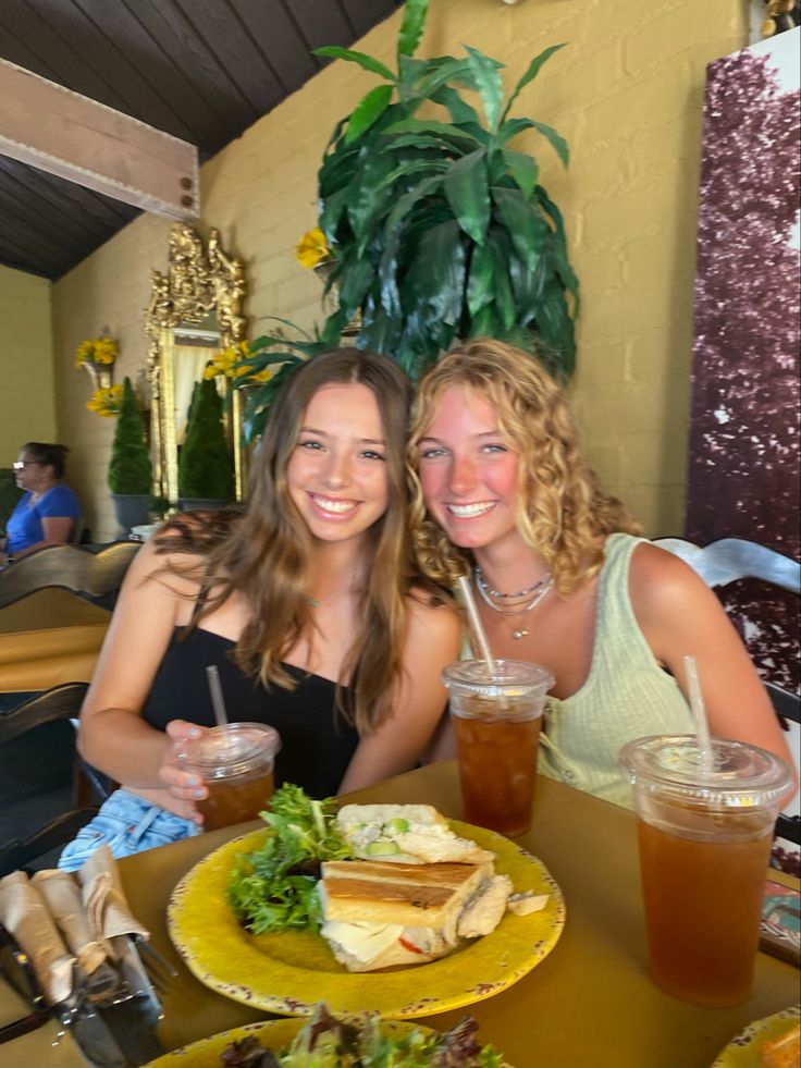 two women sitting at a table with food and drinks