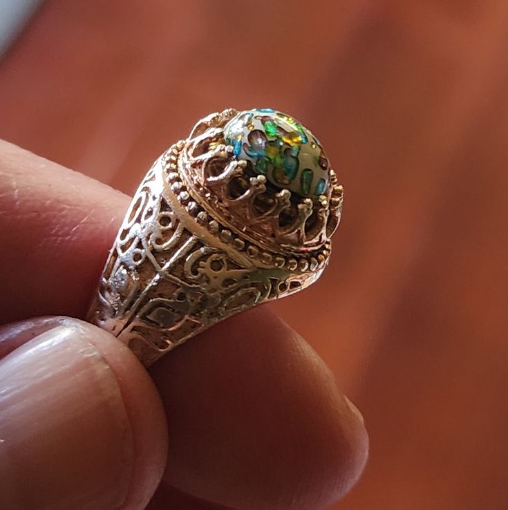 An ornate and magical looking ring! The ring is  fine sterling silver with a light wash of 14K rose gold, and there are deeply engraved foliate patterns on the shoulders. The domed cabochon is vintage Cherry Brand* confetti glass. The white glass base is overlaid with iridescent blue, lavender, green, and yellow foils. The cabochon in its setting is about 9mm high. This is a substantial, eye-catching ring with a hand-set glass cabochon. The ring is stamped '925' and contemporary. The vintage gla Vintage Cabochon Rings For Gifts, Antique Cabochon Emerald Ring Gift, Iridescent Cabochon Ring As Gift, Unique Cabochon Opal Ring For Collectors, Antique Filigree Cabochon Ring Gift, Artisan Rings, Gold Wash, Gold Vermeil, Statement Rings