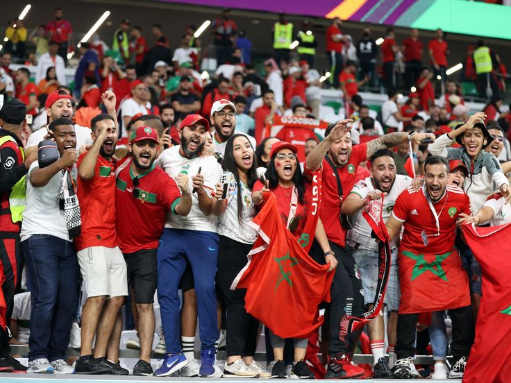 a large group of people in red and white shirts at a sporting event with flags