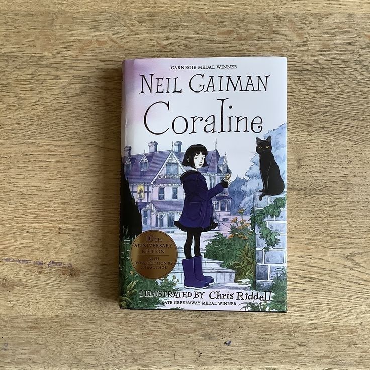 a book about coraline is sitting on a wooden table next to a black cat