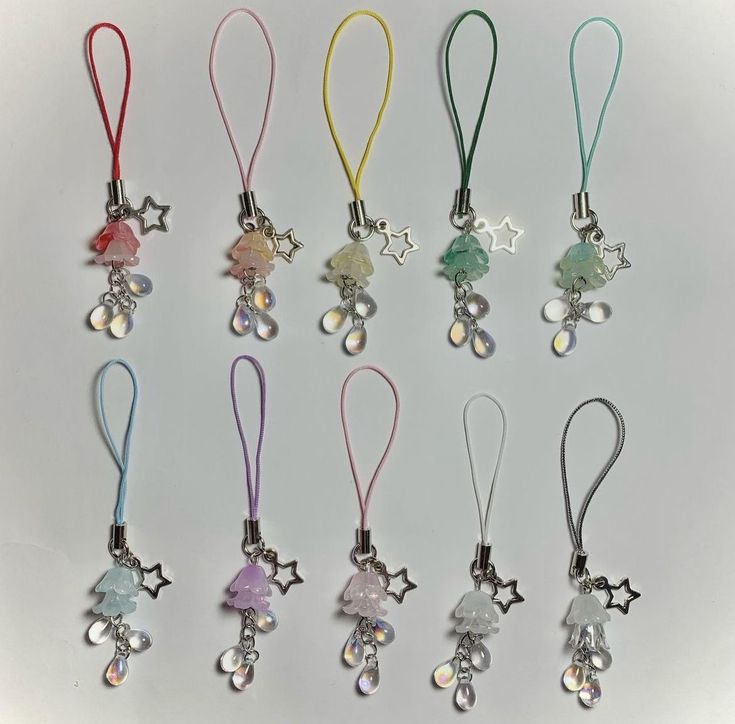 six different colored necklaces with charms hanging from them on a white surface, one has a star and the other has an elephant