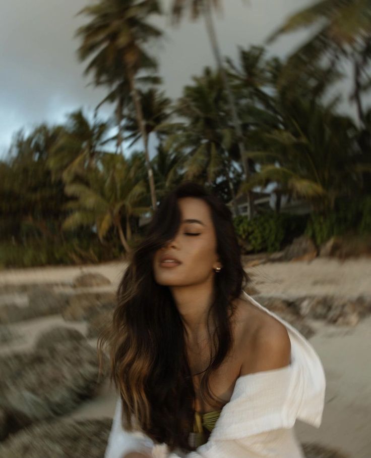 a woman standing on the beach with palm trees in the background