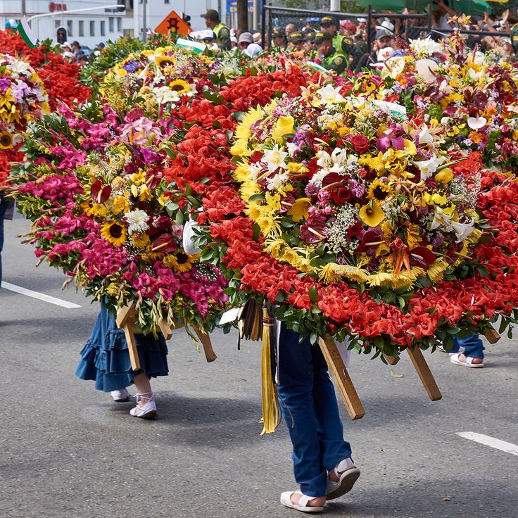 two women carrying large bouquets of flowers on their backs down the street in a parade